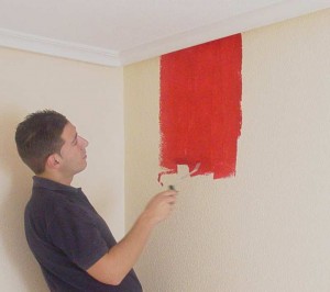 Mann streicht Wand mit roter Farbe.